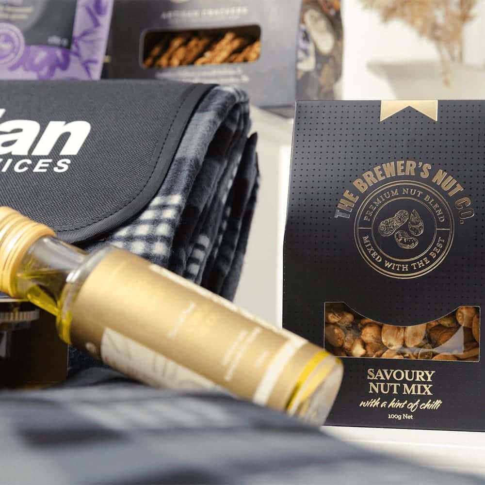A drink bottle, a picnic blanket, and a Savoury Nut Mix packaged in a black box. The blanket features a checkered pattern.