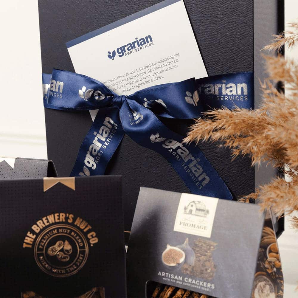 A gourmet picnic gift pack featuring artisan crackers, gourmet nuts, and a decorative box with a blue ribbon and branding.