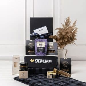 A picnic gift pack featuring a drink bottle, gourmet snacks, honey, and a checkered blanket in blue and black tones.