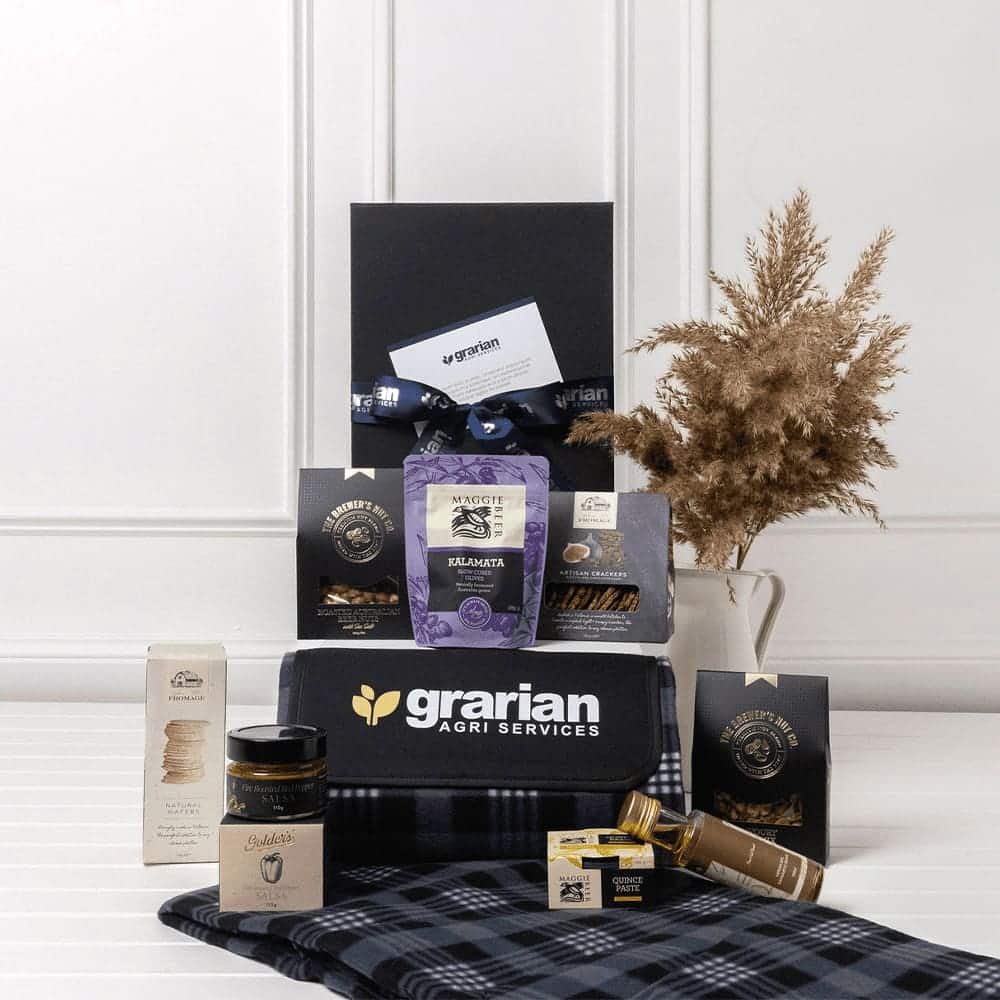 A picnic gift pack featuring a drink bottle, gourmet snacks, honey, and a checkered blanket in blue and black tones.