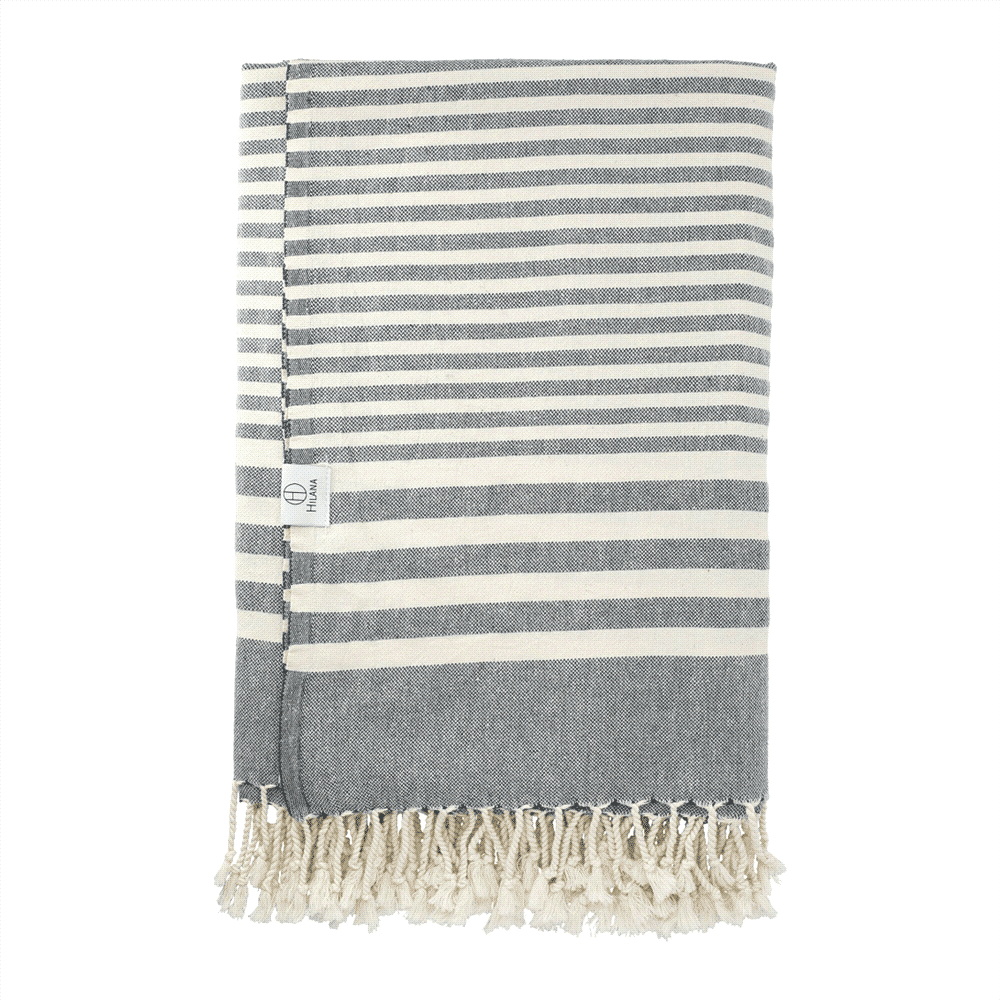 A grey and white striped blanket with tassel detailing, featuring a small logo tag.