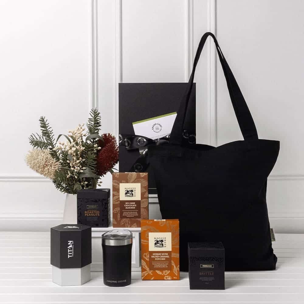 A black tote bag with assorted sweet treats, essential items, and a decorative floral arrangement.