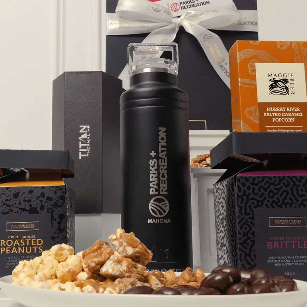 A black drink bottle surrounded by popcorn, roasted peanuts, and brittle in elegant packaging.