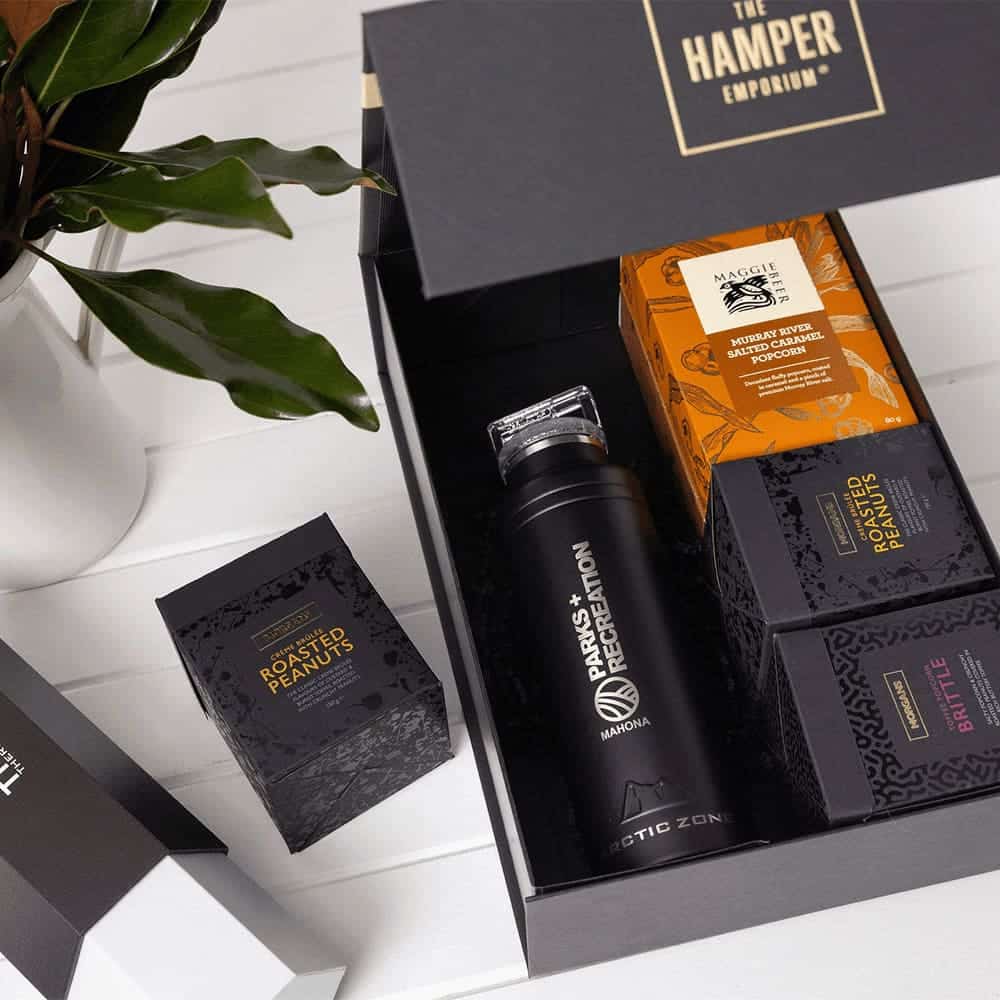 A drink bottle and assorted snack boxes, including roasted peanuts, in a black gift pack with a logo.