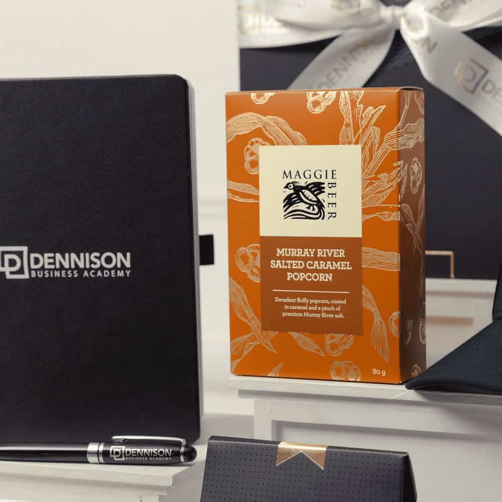 A gift pack featuring a black notebook, a silver pen, a black cap, and orange popcorn packaging.