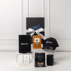 A gift pack featuring a black cap, notebook, candle, and assorted packaged items, all presented in a sleek box with a bow.