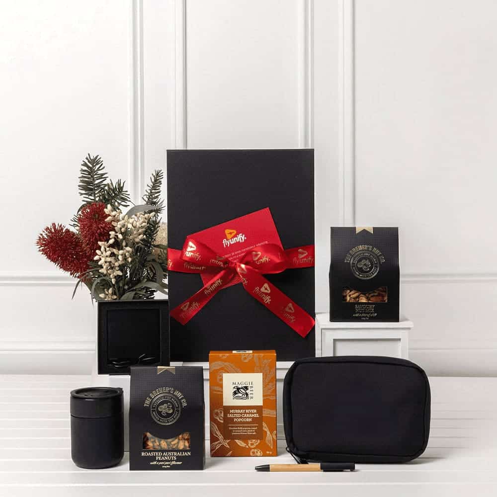 A black gift box tied with a red ribbon, containing coffee packets, a black mug, a pouch, and a pen.