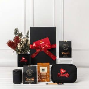 A black gift box tied with a red ribbon contains various items, including a drink bottle, a coffee pack, and a branded pouch.