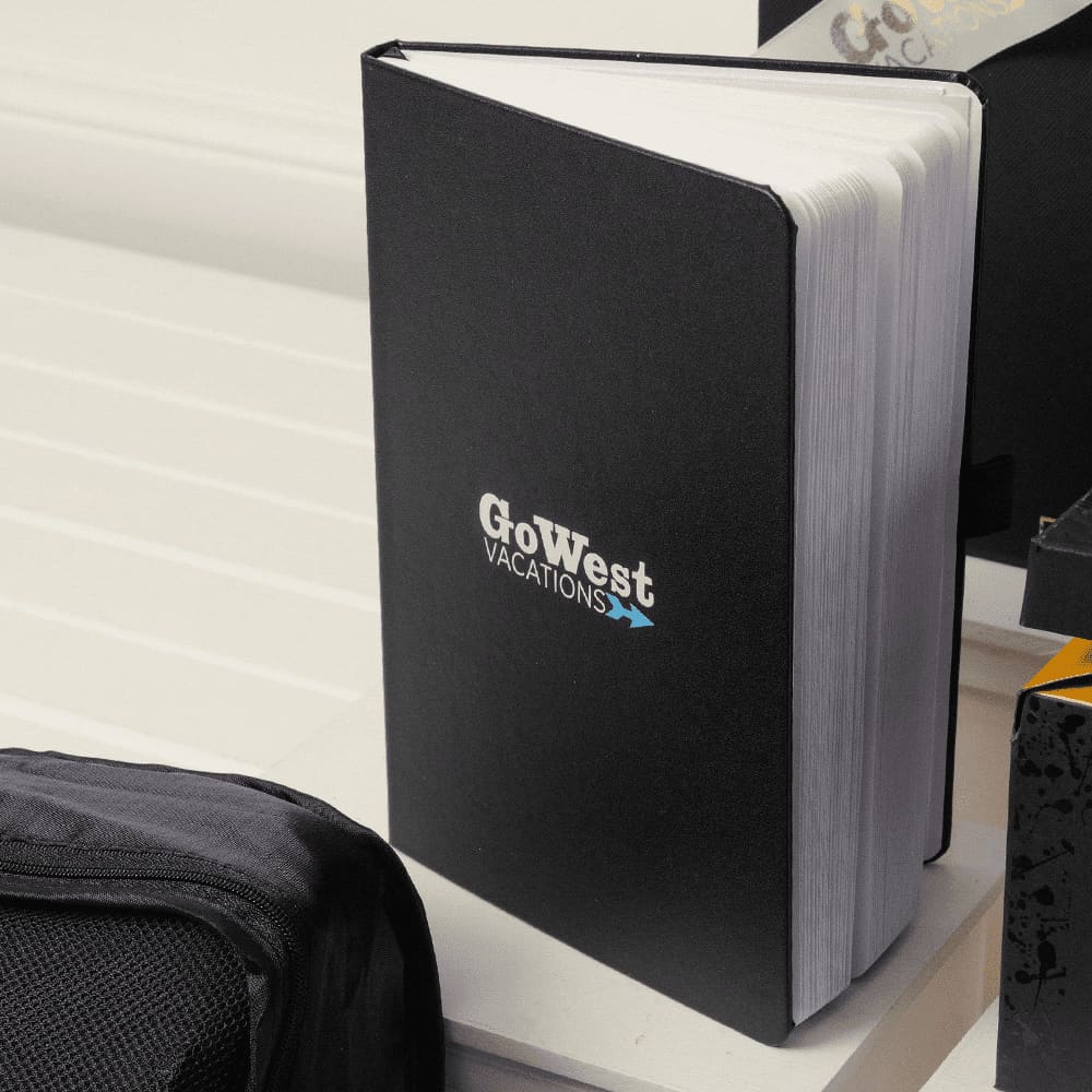 A black notebook with a logo, featuring blank pages, rests on a white surface alongside other items.