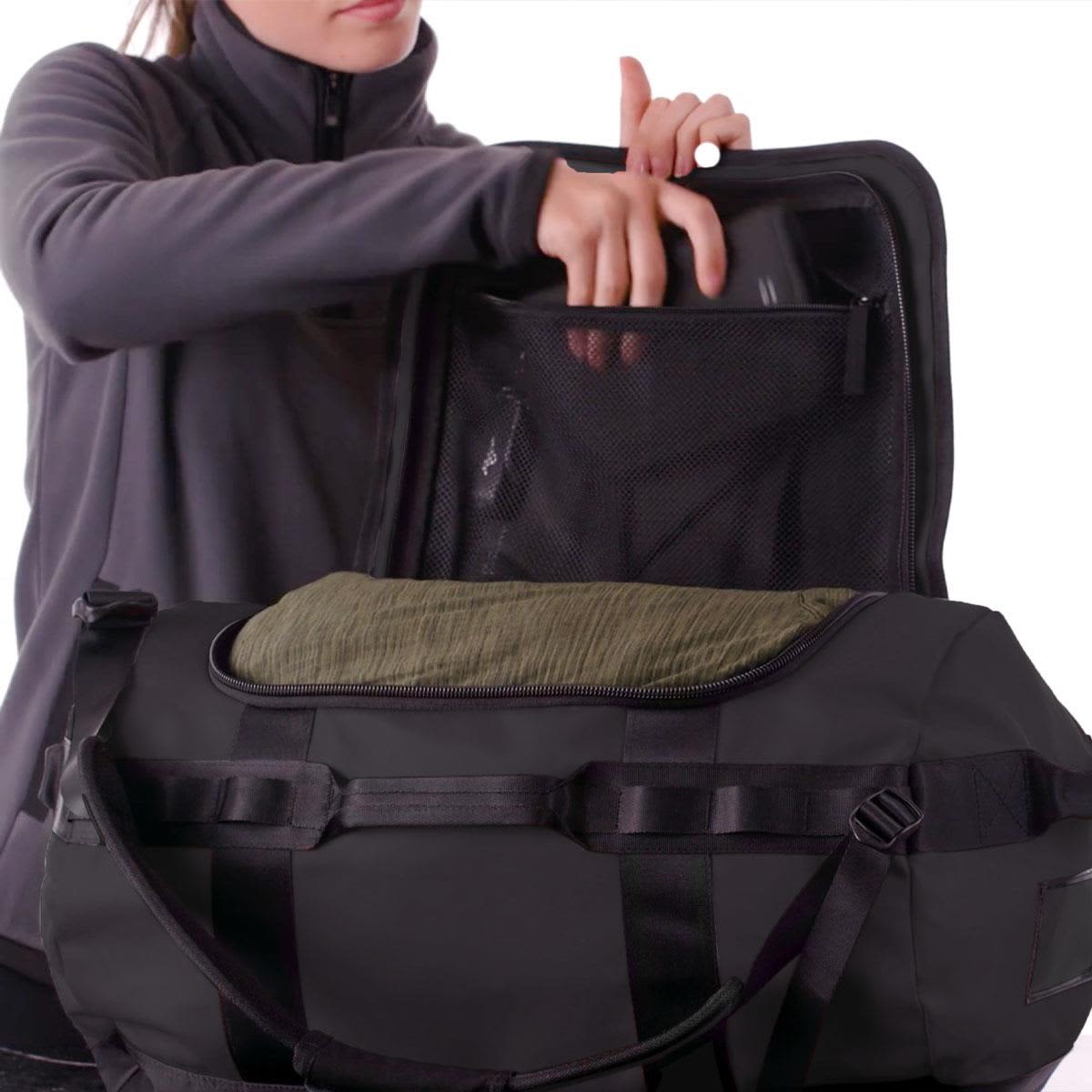 A black duffle bag with a mesh pocket and a rolled green item inside, being held by a person in a grey jacket.