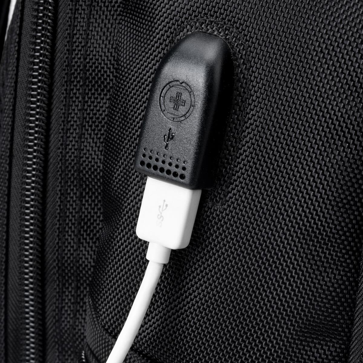 A close-up of a black backpack featuring a USB port and a white cable connected to it.
