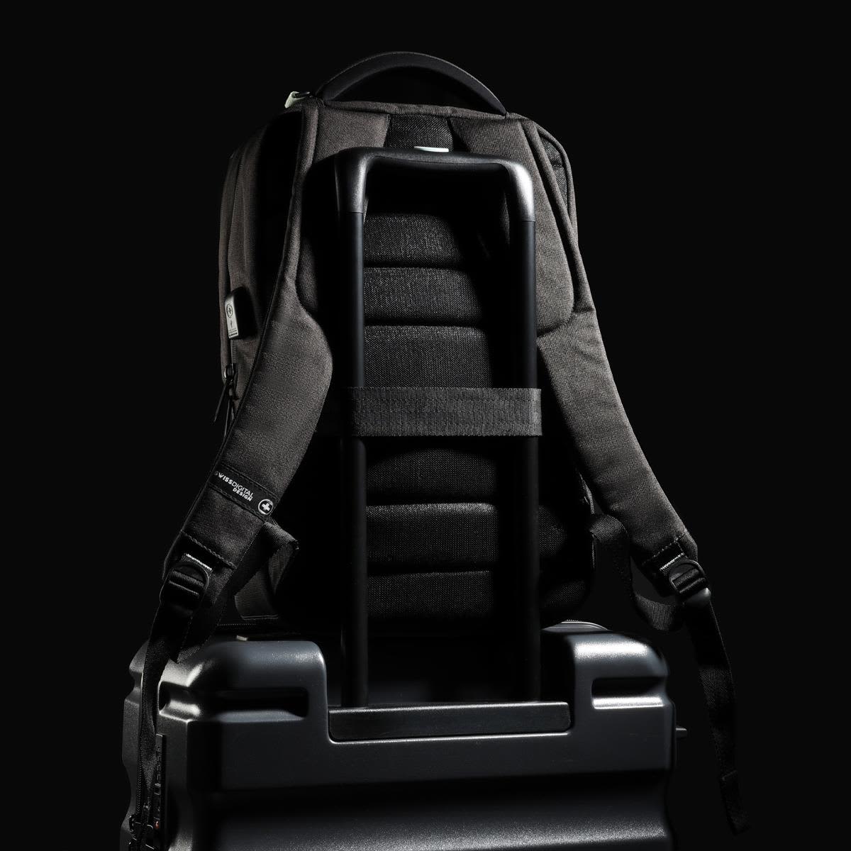 A black Swissdigital Arosa Backpack rests on a suitcase, featuring straps and a sleek design.