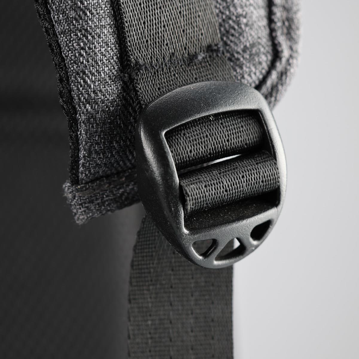 A close-up of a black buckle and strap on a grey backpack, featuring fabric detailing and stitching.