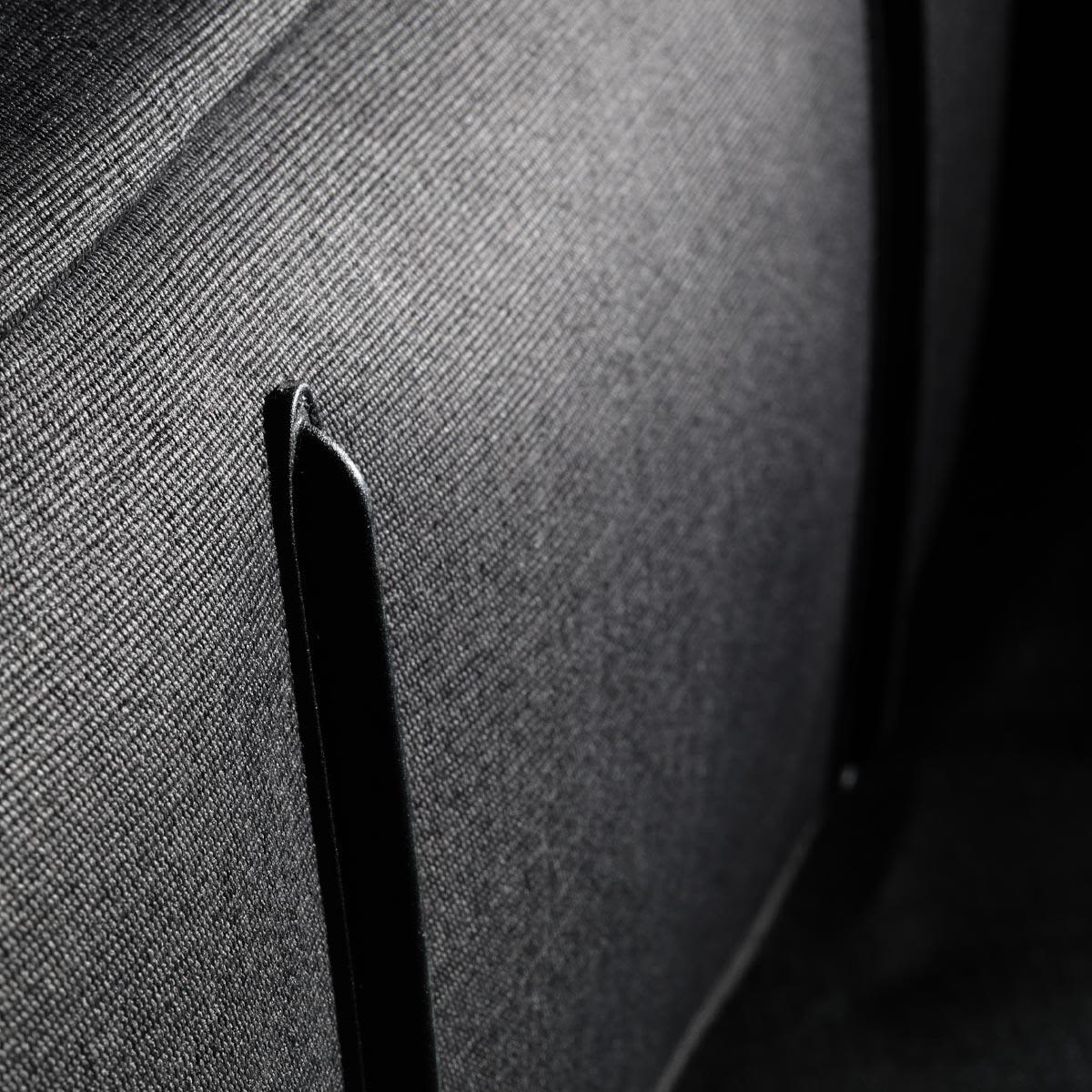 A close-up of fabric showing a textured black surface with a black trim detail. The material appears durable and structured.
