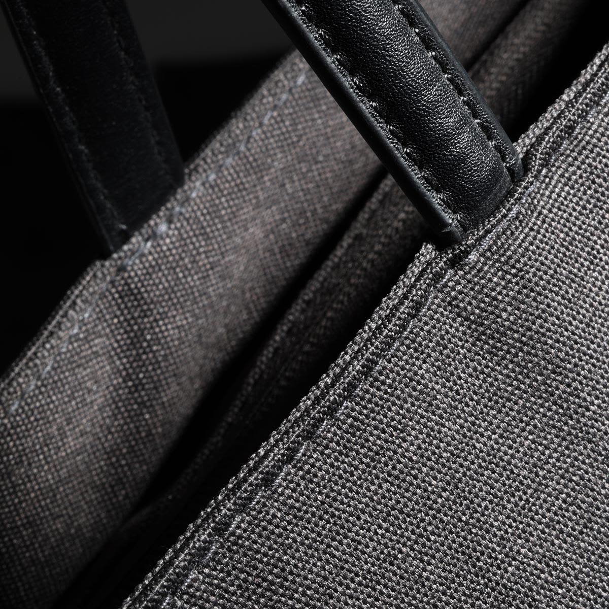 A grey tote bag featuring dark green leather handles and stitching, with a close-up view of the fabric texture.