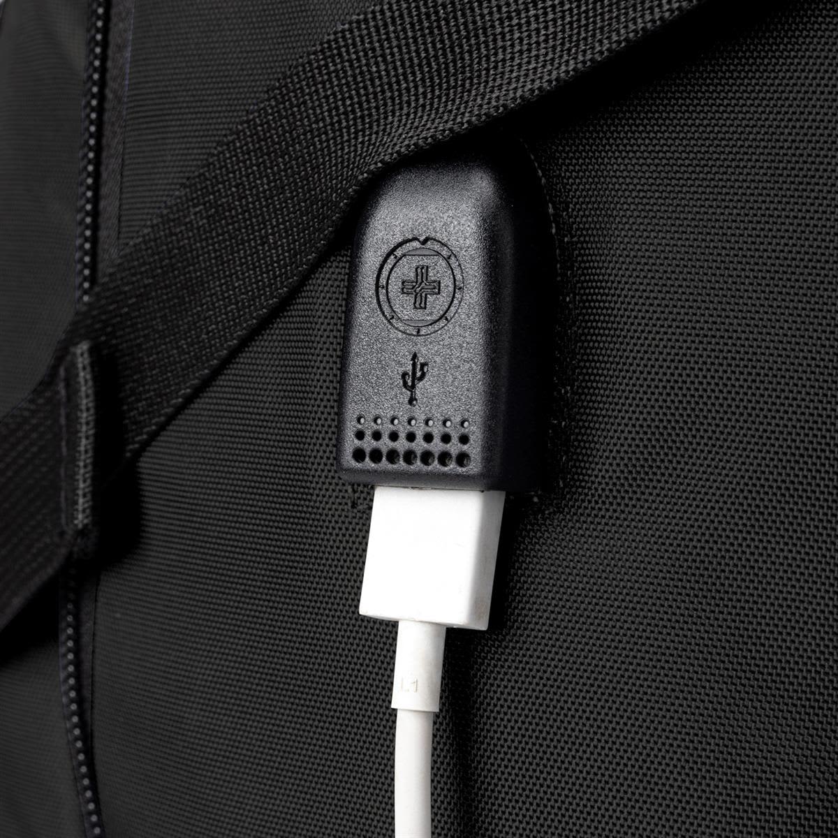A close-up of a black backpack with a USB charging port and cable attached. It features a textured strap.