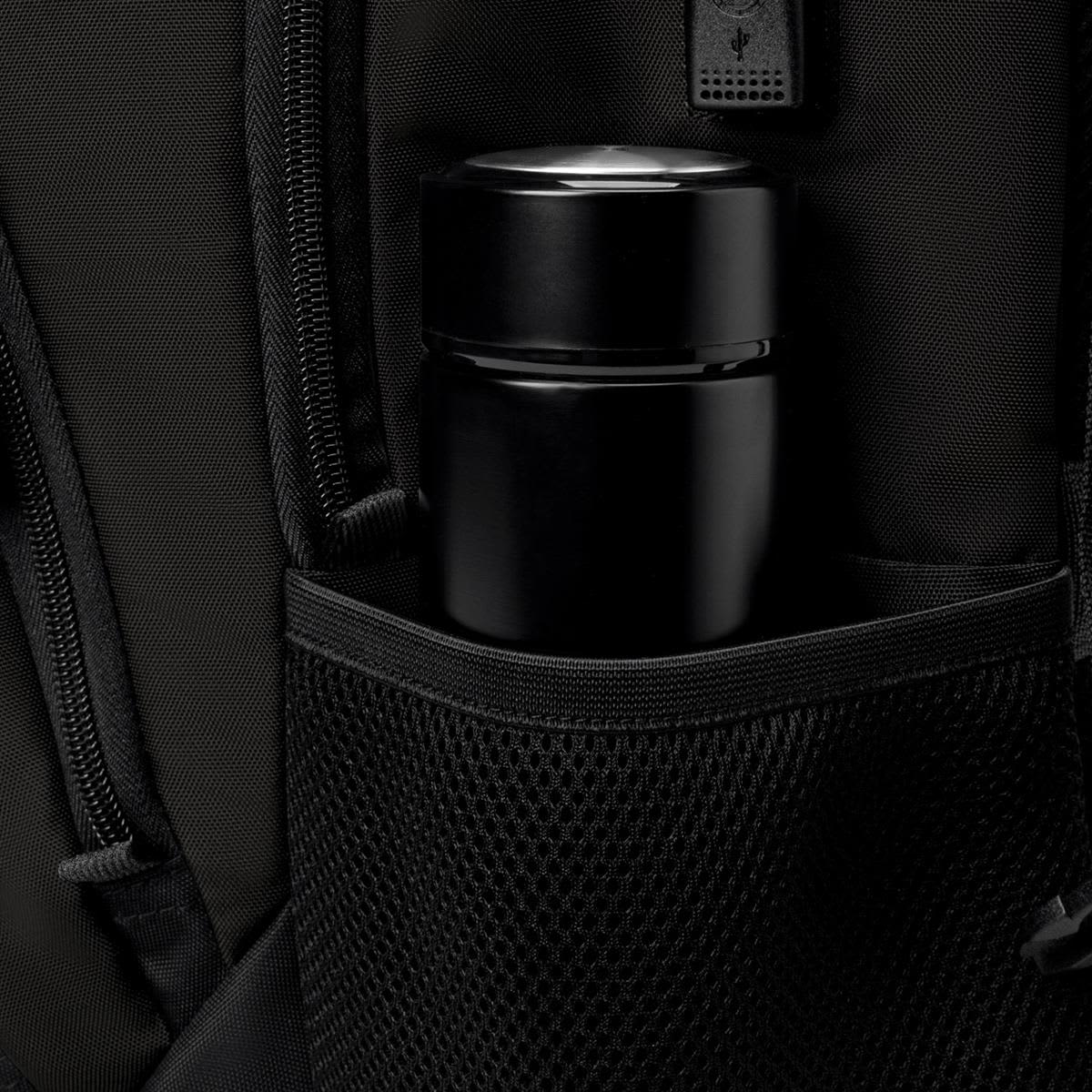 A black thermos is nestled in a mesh pocket of a black backpack featuring various zippers and compartments.