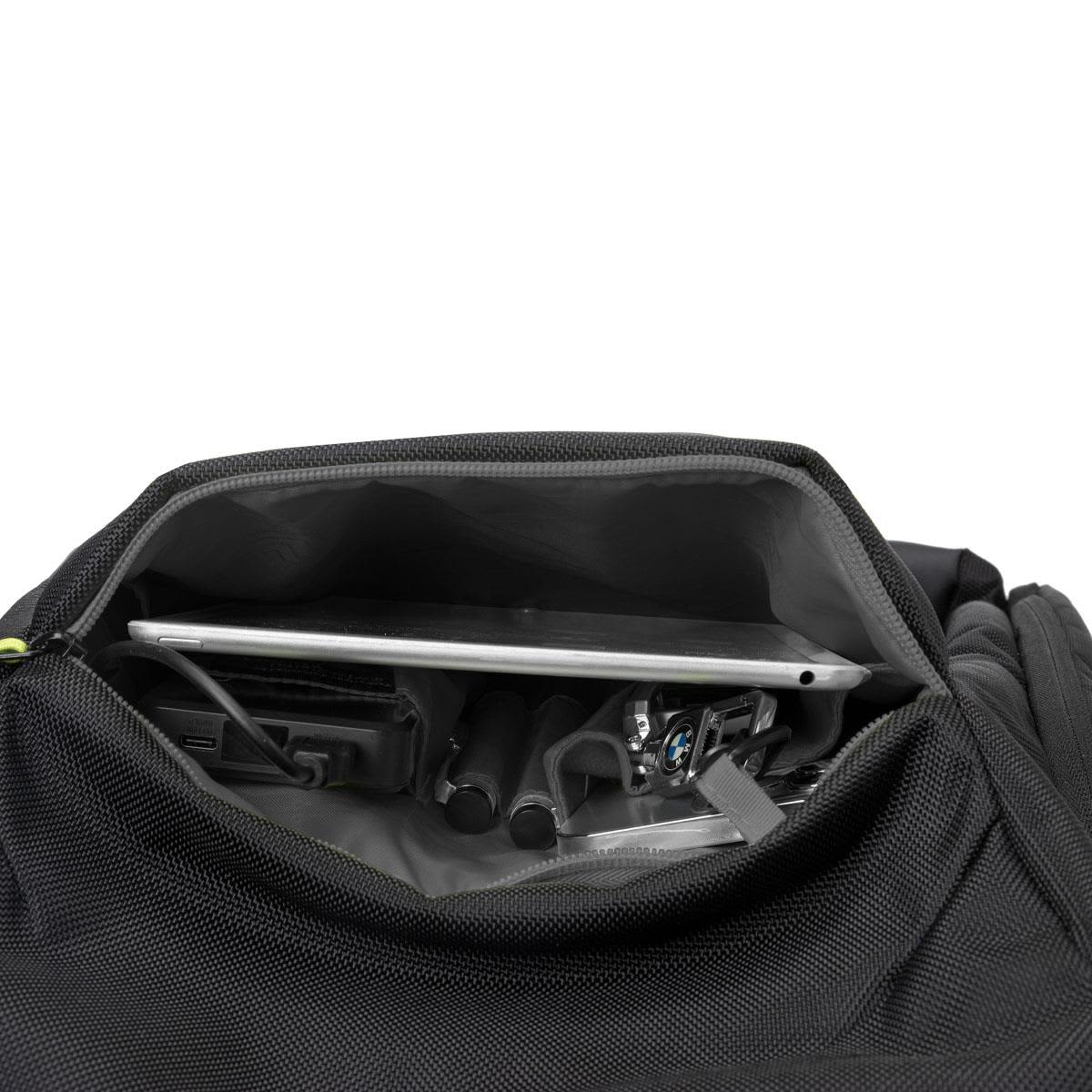 An open black backpack revealing a laptop, cables, and other accessories inside. It features a logo.