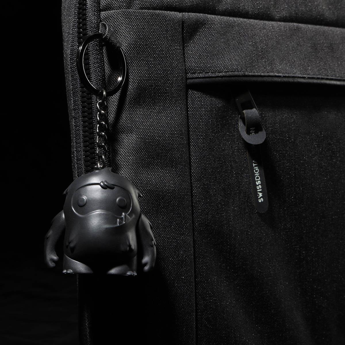 A black laptop sleeve features a textured surface and a keychain with a small black character.