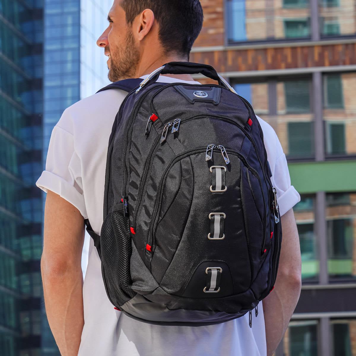 A black backpack with red accents, featuring multiple compartments and a logo, worn by a person outdoors.