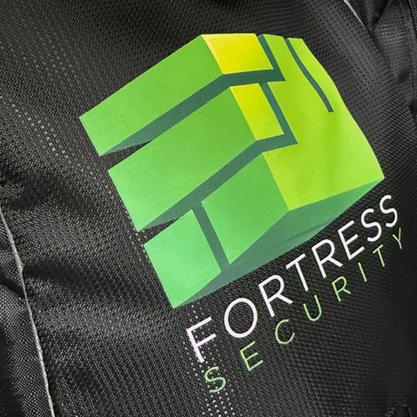 SupaDTF printed geometric fortress logo in shades of green, applied to a black nylon backpack for Fortress Security branding.