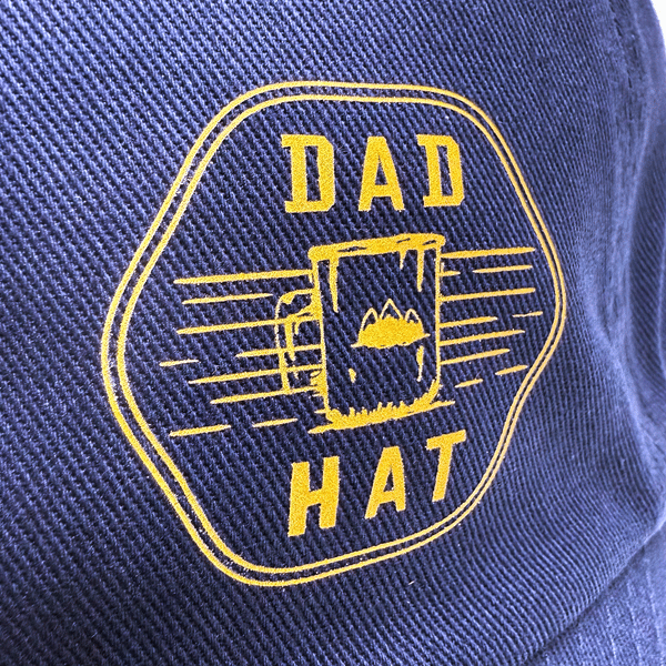 Navy dad hat with bold yellow “DAD HAT” and mug design printed using SupaDTF on textured cotton twill, emphasising crisp contrast.