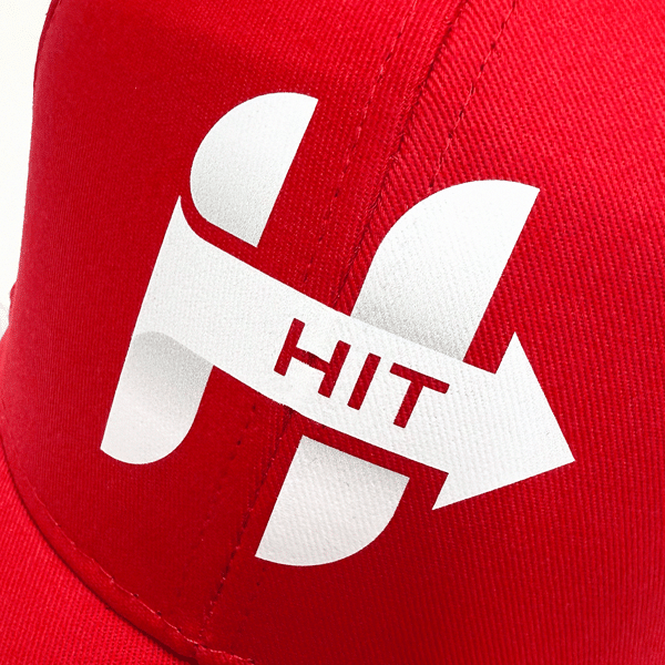 Red promotional cap featuring white SupaDTF arrow logo and "HIT" text, highlighting the precision and durability of digital transfer prints.