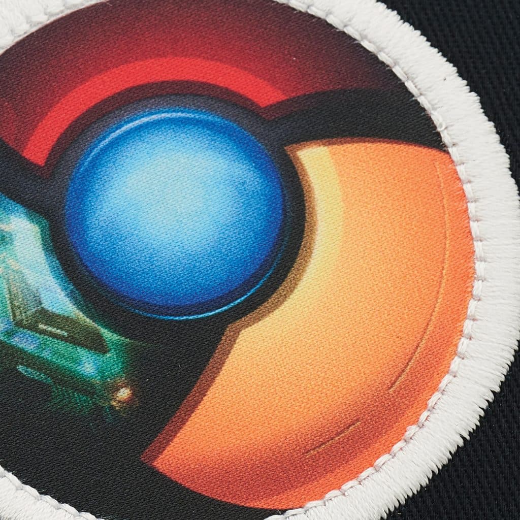 Close-up of a vibrant embroidered patch featuring a circular, multicoloured design with a glowing blue centre, applied to dark fabric—showcasing premium Supasub decoration.
