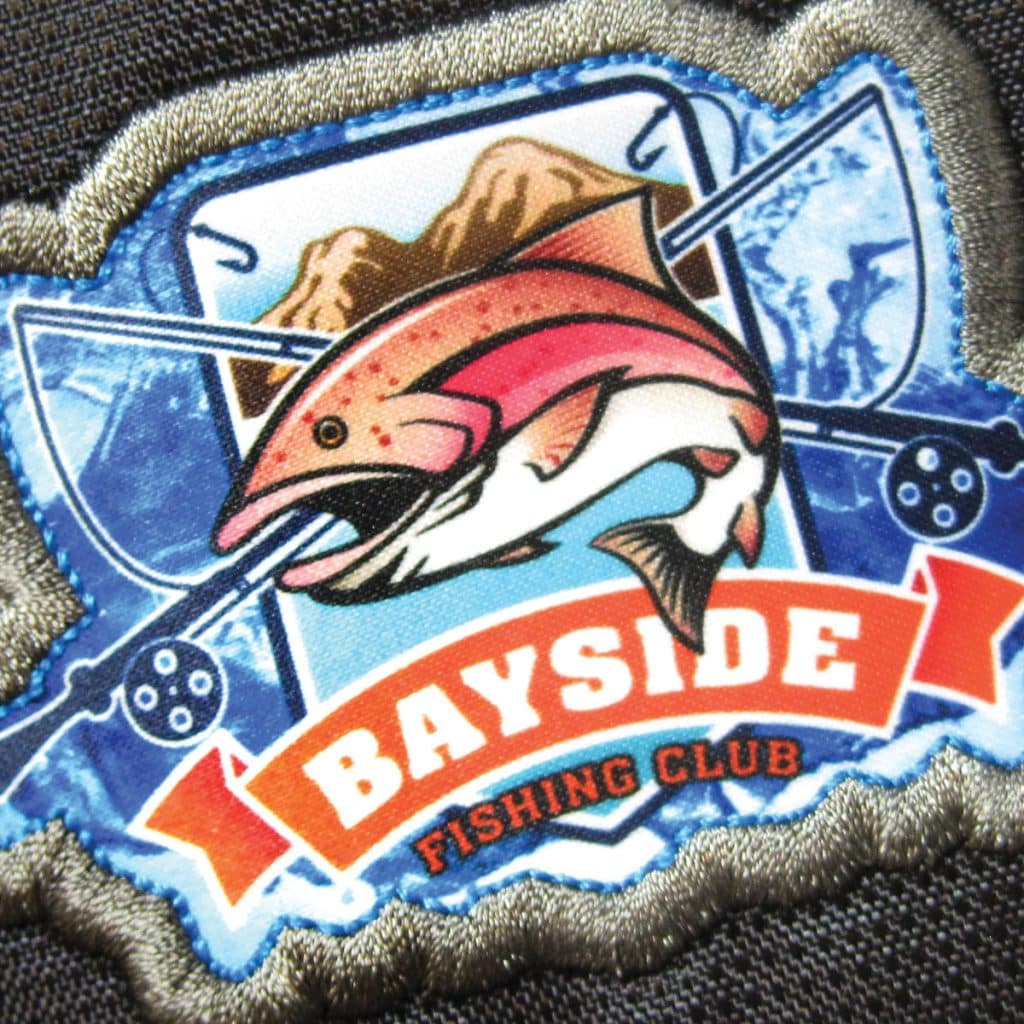 Fishing-themed patch with a pink salmon, rods, and “Bayside Fishing Club” text on a textile surface, ideal for hobby-based best branded merchandise.