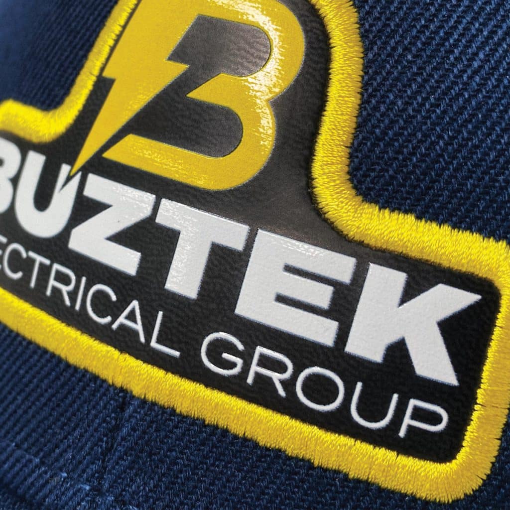 Badge displaying Buzztek Electrical logo on a black cap, with gloss print and stitched white border.
