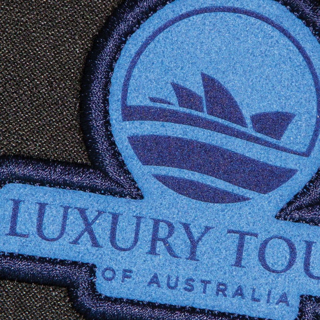 Suede-texture patch in navy and blue with Sydney Opera House silhouette and "Luxury Tours of Australia" branding.