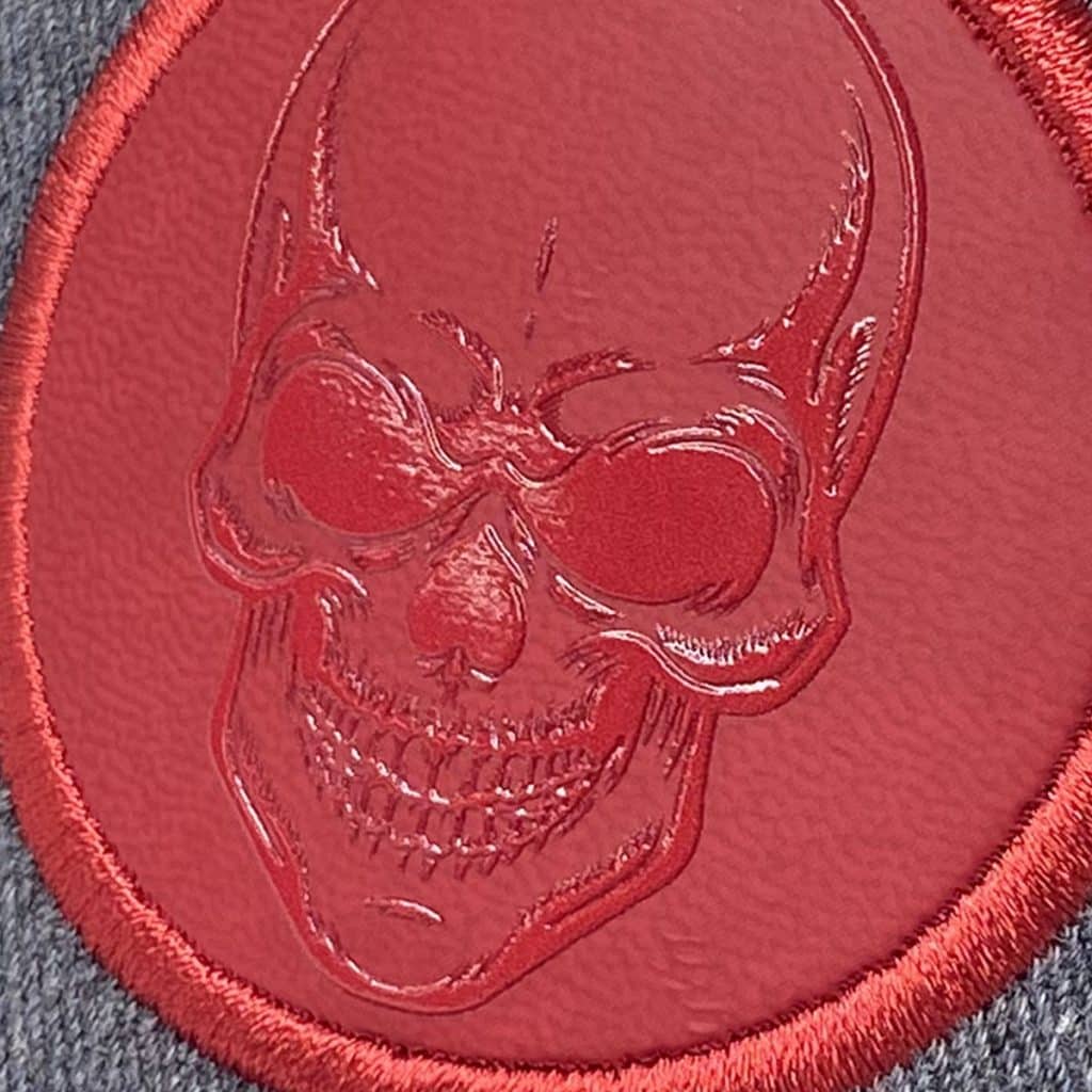 Supaflex badge featuring red gloss skull design on matte background, printed on flexible substrate with stitched rim.