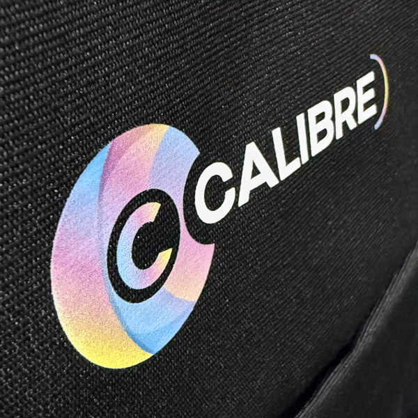 SupaDTF print of Calibre’s circular logo with pastel gradient overlays on black polyester, showing fine edge detail and smooth texture.