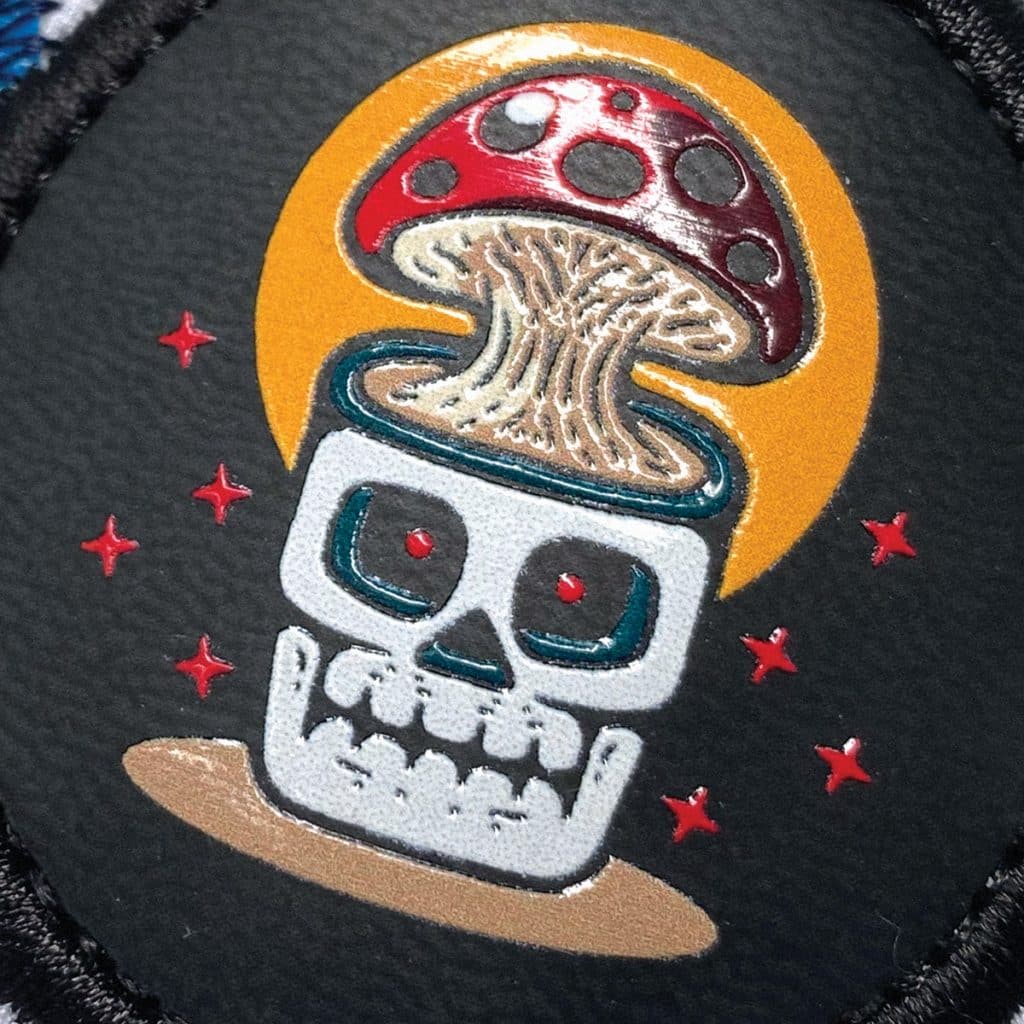 Badge with skull and mushroom artwork in full colour, stitched onto black base for high visual contrast.