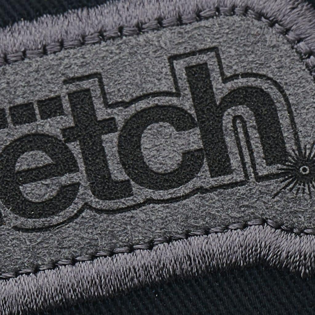 Close detail of black-on-grey SupaEtch logo with stitching and fine laser-cut texture.