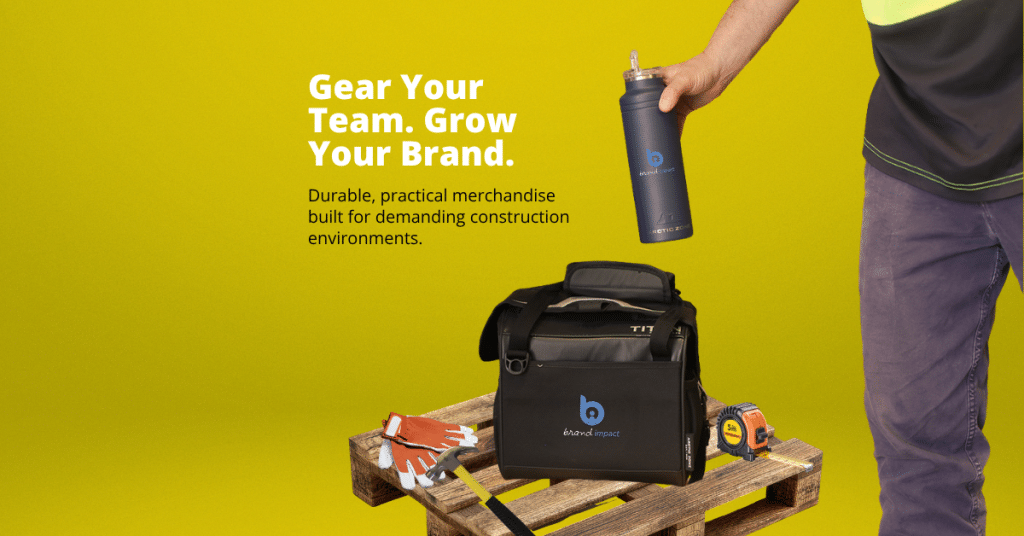 Construction-themed promotional merchandise banner featuring a branded insulated drink bottle, rugged cooler bag, work gloves and tape measure on a timber pallet, with a worker reaching for the bottle. The banner includes the headline “Gear Your Team. Grow Your Brand.” and promotes durable, practical branded merchandise designed for demanding construction environments.