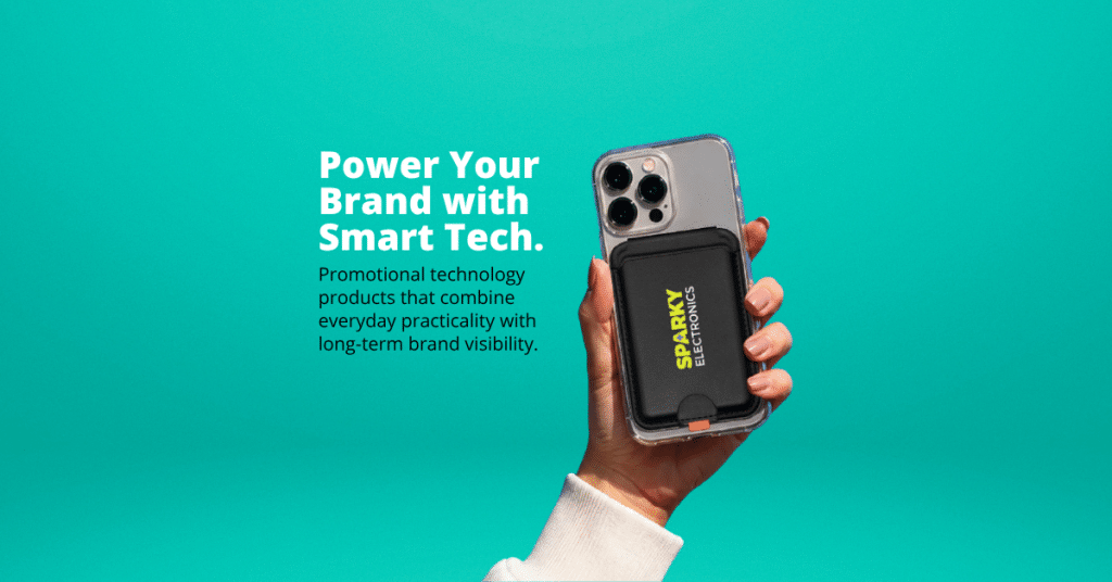 Hand holding a smartphone with a branded magnetic power bank attached to the back against a teal background, alongside the message "Power Your Brand with Smart Tech," highlighting promotional technology products that combine everyday practicality with long-term brand visibility.