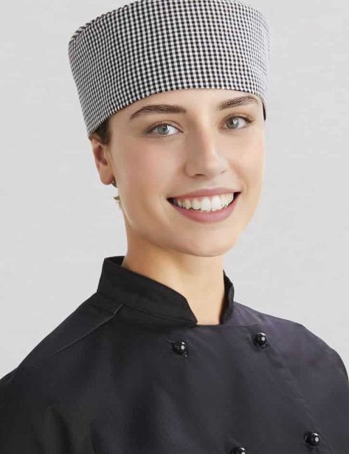 A chef cap in a black and white checkered pattern, worn by a smiling individual in a black chef's uniform.