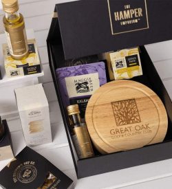 A gourmet gift set featuring a wooden board, various condiments, snacks, and a branded box. Includes purple and gold packaging.