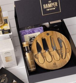 A gourmet gift pack featuring a bamboo cheese board set, assorted snacks, and a selection of condiments in a black box.