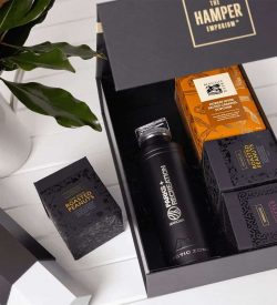 A drink bottle and assorted snack boxes, including roasted peanuts, in a black gift pack with a logo.