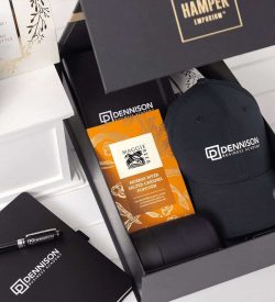 A black cap, a pen, and gourmet popcorn in an elegantly designed gift box featuring a logo.