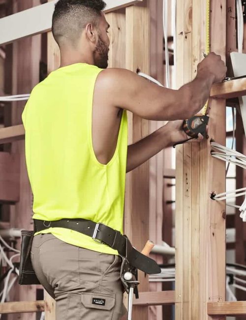 A man wearing a fluorescent yellow sleeveless tee is working with tools in a construction setting.